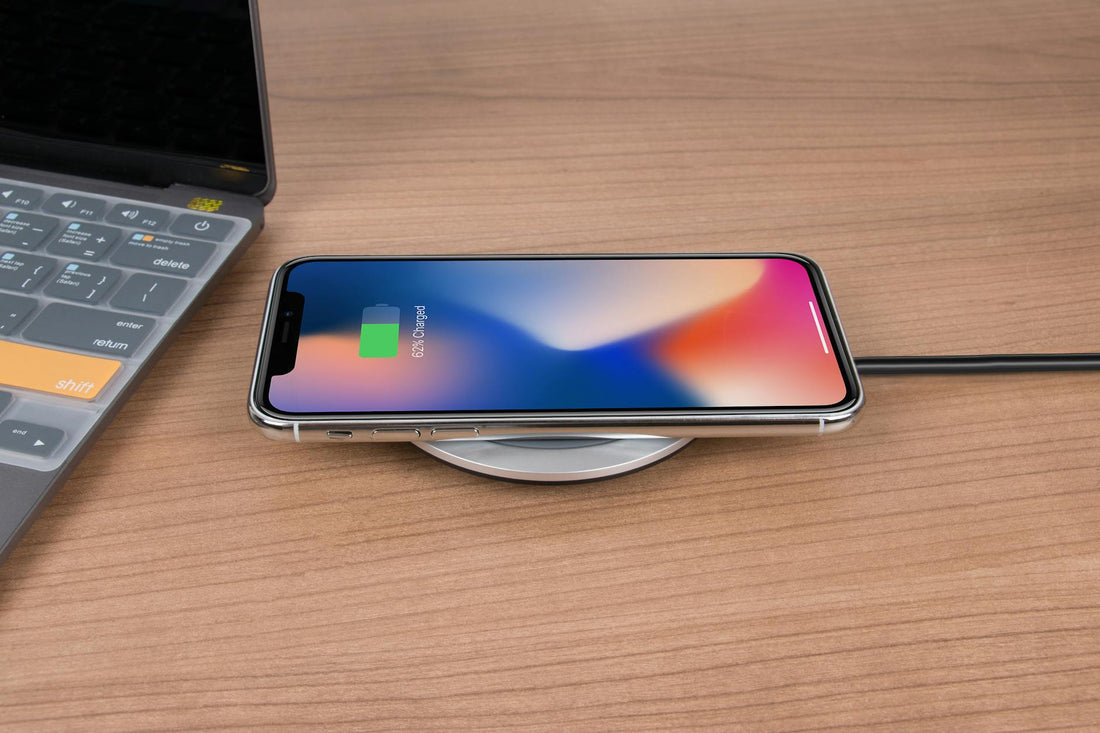 Mobile phone charging wirelessly on a desk next to a laptop, showcasing modern technology.